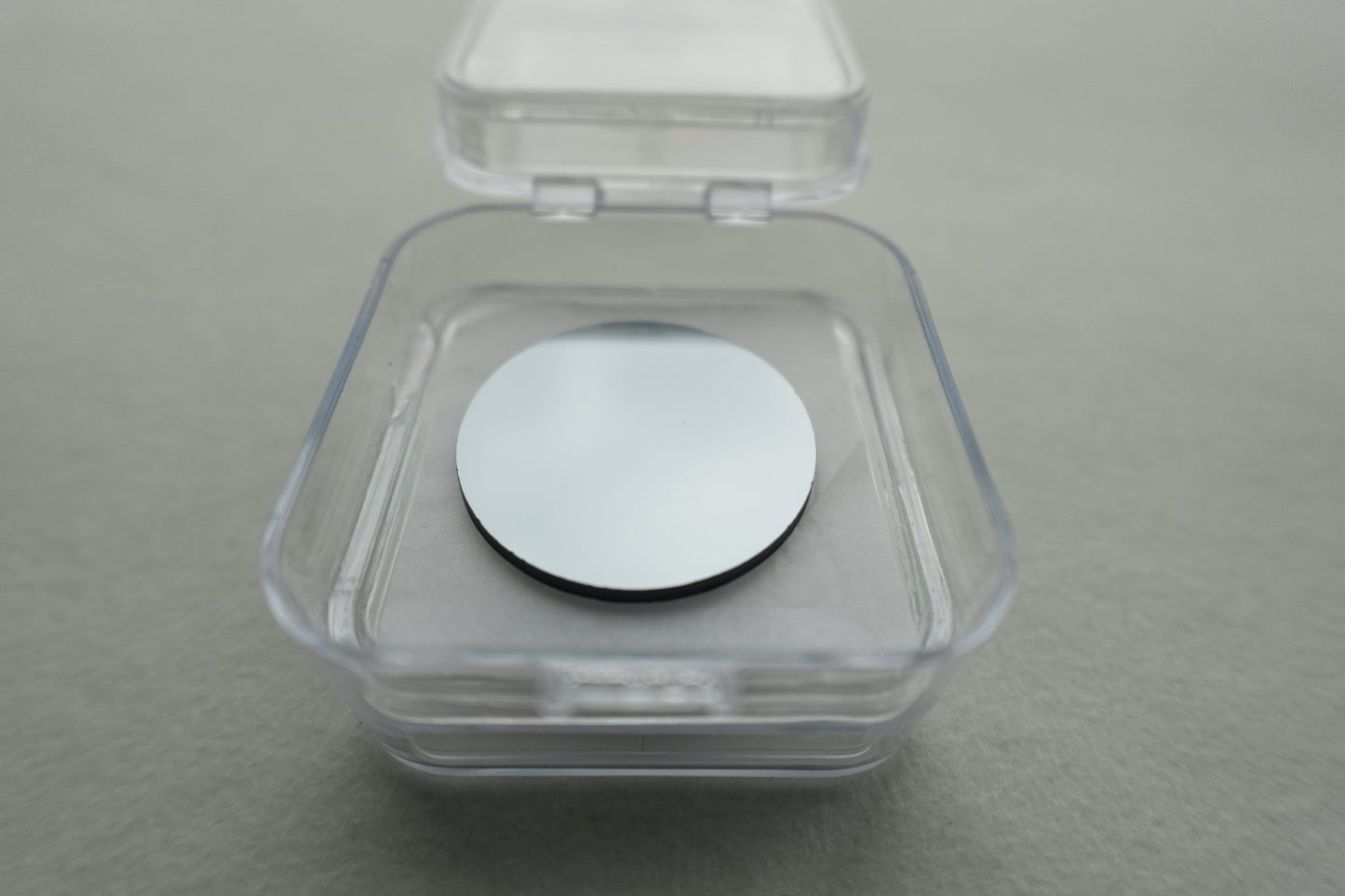 Silver round sample holder in open clear plastic Panalytical box on gray background
