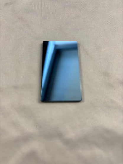 Small rectangular mirror reflecting a blue window frame on beige fabric surface