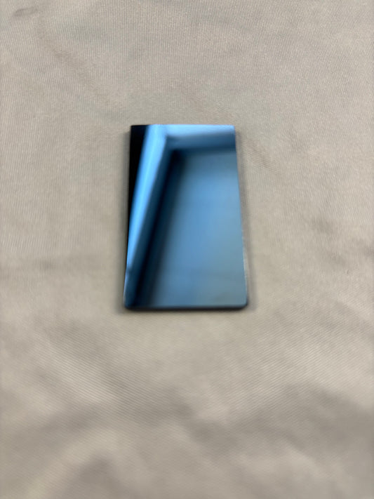 Small rectangular mirror reflecting a blue window frame on beige fabric surface
