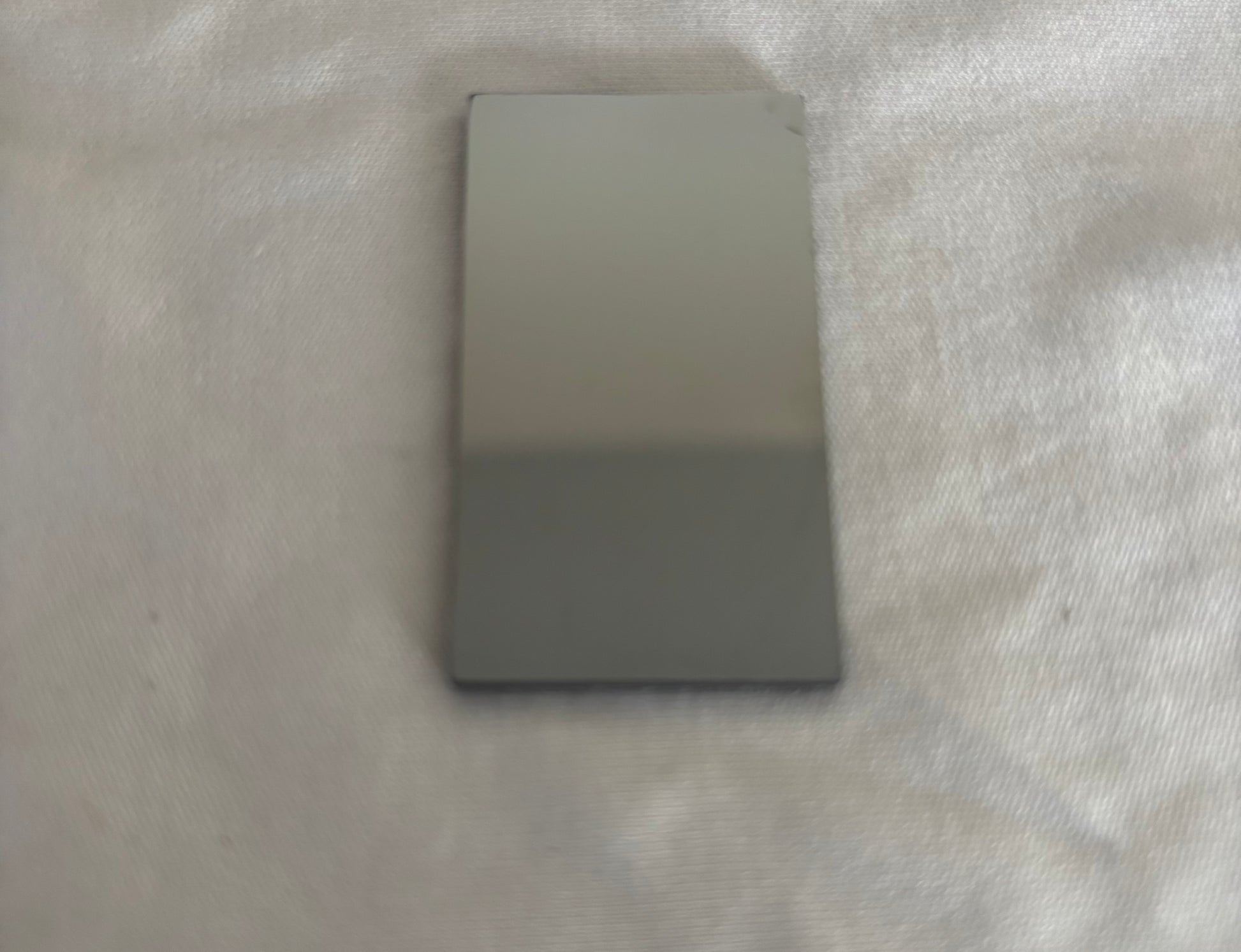 Rectangular glossy gray ceramic tile on textured fabric surface