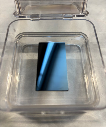 Reflective black rectangular object inside an open transparent plastic container on white fabric